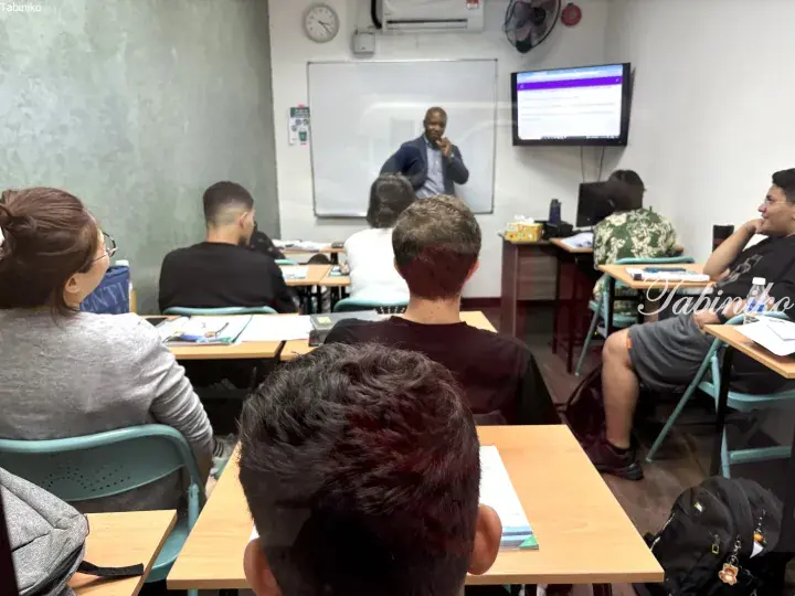 Students attentively watching a presentation in a classroom with a whiteboard and TV screen.