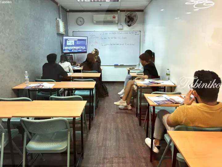 Students in a classroom learning English grammar from a whiteboard and digital screen at a language center.