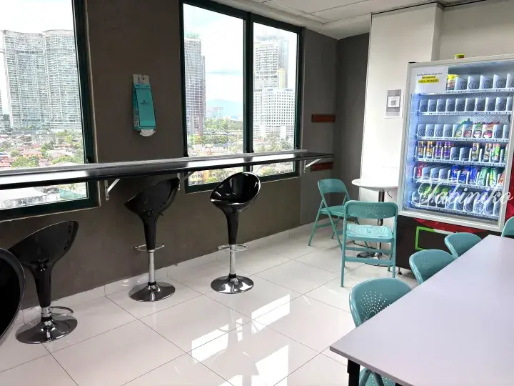 Modern lounge with black bar stools and vending machine overlooking Kuala Lumpur high-rise buildings.