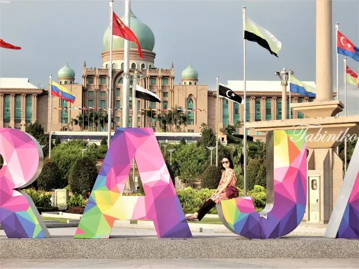 Colorful geometric letters spelling ‘KUALA LUMPUR’ with a woman sitting on the ‘U’ and the Prime Minister’s Office in the background.
