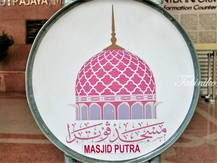 Circular sign featuring a pink dome illustration and text for Masjid Putra, a mosque in Putrajaya, Malaysia.