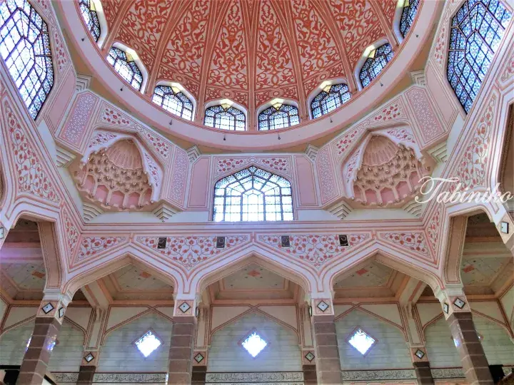 Pink mosque interior featuring intricate geometric patterns, stained glass windows, and ornate domed ceilings.