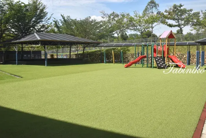 Children’s playground with slides and climbing wall on green artificial turf under a shaded pavilion at a Malaysia property.