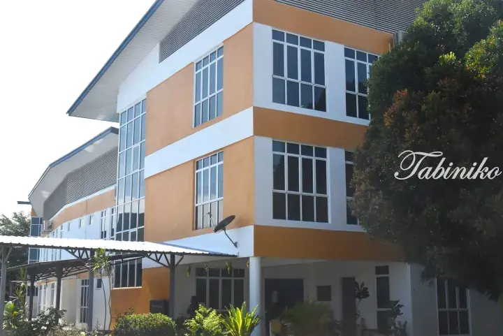 Modern orange and white multi-story building with large windows and a satellite dish, surrounded by lush greenery.