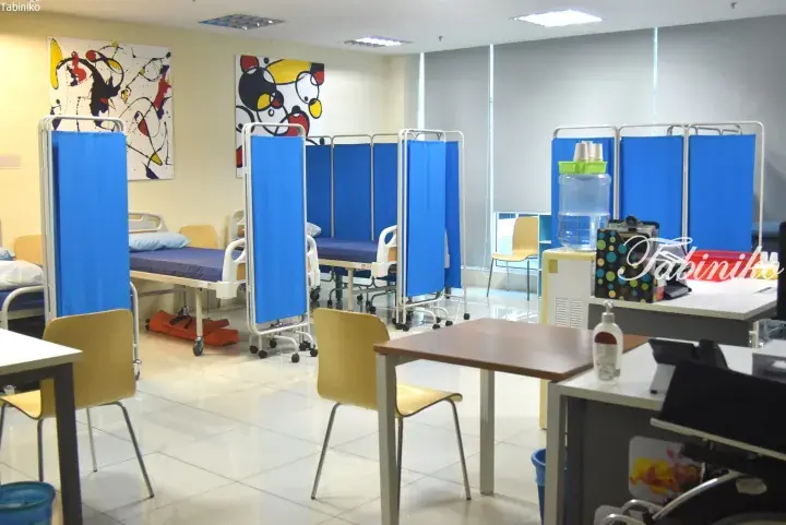Clean hospital ward with blue privacy curtains, beds, and modern abstract wall art.