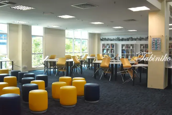 Bright library study area with yellow chairs, blue and yellow stools, and bookshelves at Epsom College in Malaysia.