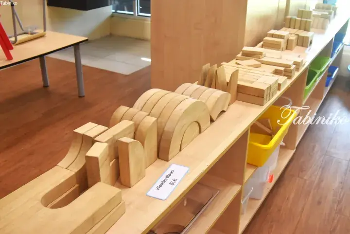 Organized wooden building blocks and arches neatly arranged on a low shelf in a bright, modern playroom.