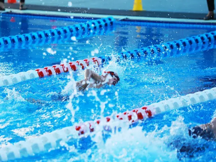 Swimmer in a pool lane performing the butterfly stroke with water splashing around.