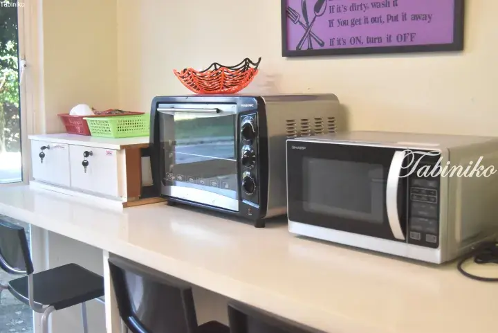Kitchen counter with a silver toaster oven and microwave, plus a sign reminding guests to keep the area clean.