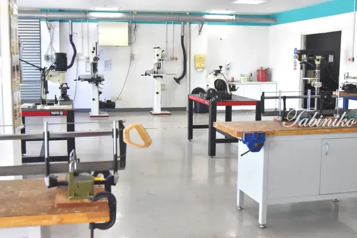Well-lit workshop with workbenches, clamps, and power tools like a drill press and bandsaw for DIY projects.