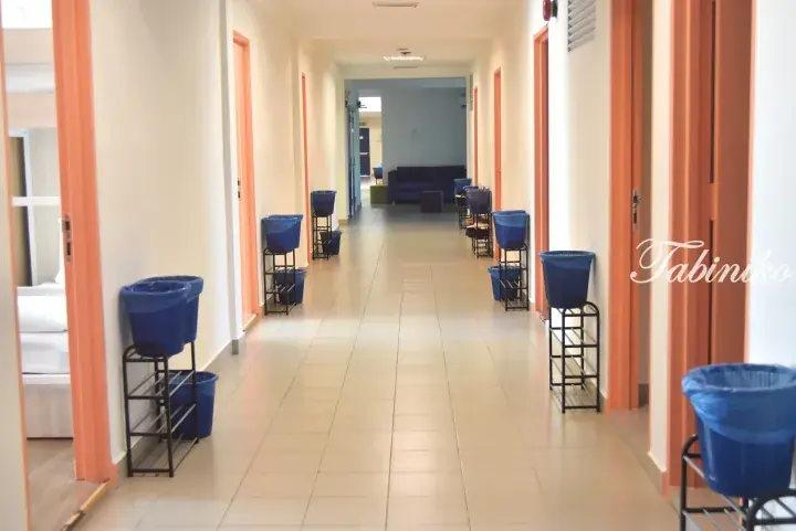 Bright dormitory hallway with blue trash bins on stands and orange door frames leading to a lounge area