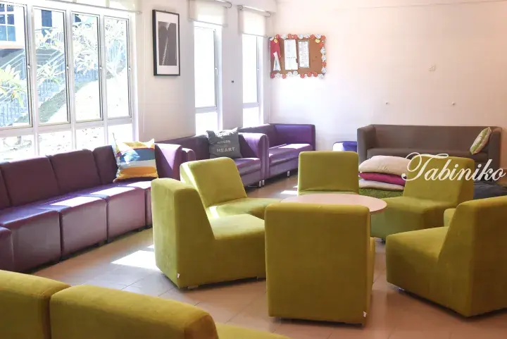 Bright student lounge with purple sofas and green armchairs arranged around a table in a modern shared accommodation space.