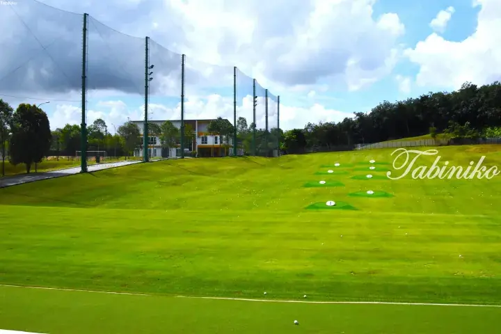 Golf driving range with numbered hitting bays and safety netting against a blue sky.