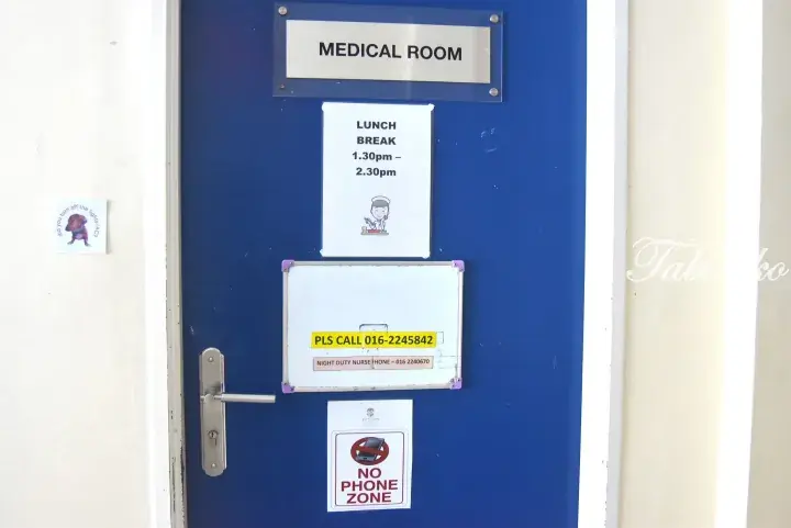 Blue door with signs for Medical Room, lunch break hours, contact numbers, and a no phone zone notice.