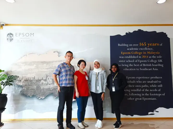 Four staff members stand smiling in front of a wall display at Epsom College in Malaysia.