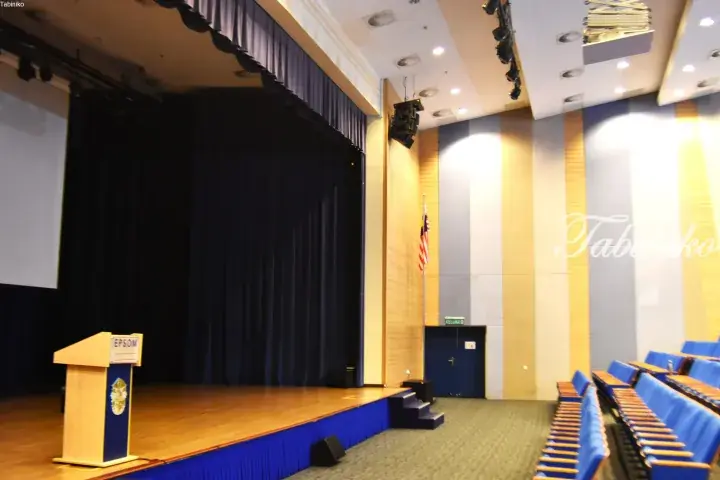 Epsom Institute auditorium stage with wooden podium, blue curtains, and rows of blue seats.