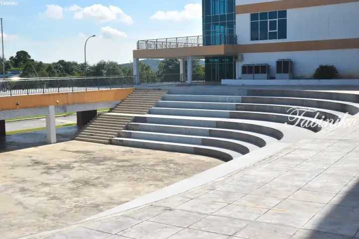 Curved concrete tiered seating steps leading to a modern building entrance with glass facade and yellow accents.