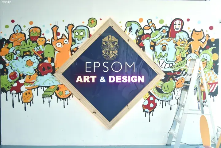 Colorful mural with cartoon characters surrounding an EPSOM Art & Design sign in a wooden frame.