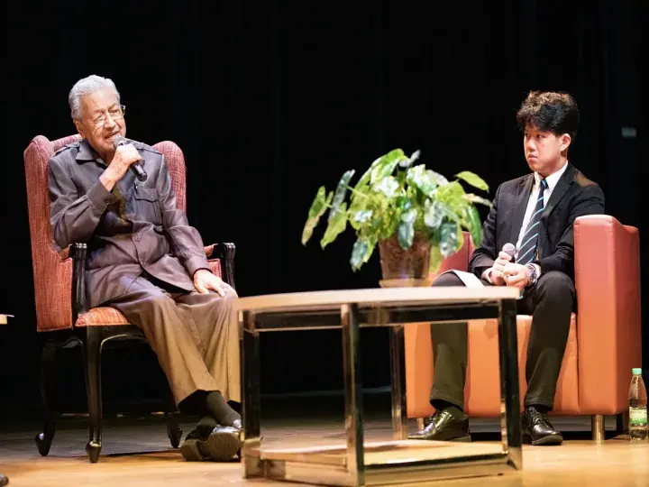 Former Malaysian Prime Minister Mahathir Mohamad speaking at a public event, seated in a red armchair on stage.
