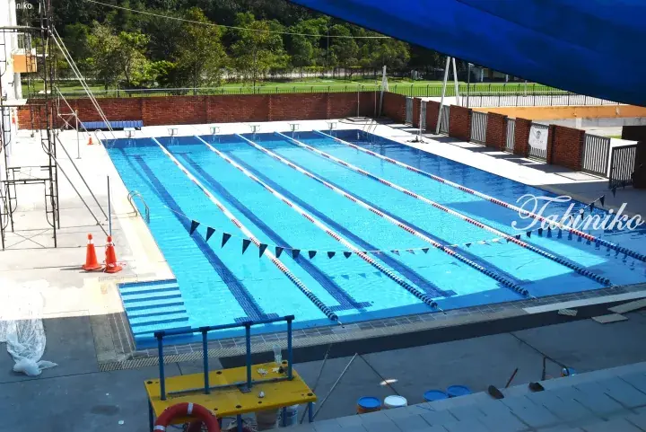 Outdoor swimming pool with six lanes, starting blocks, and a yellow lifeguard chair under a blue shade at a school facility.