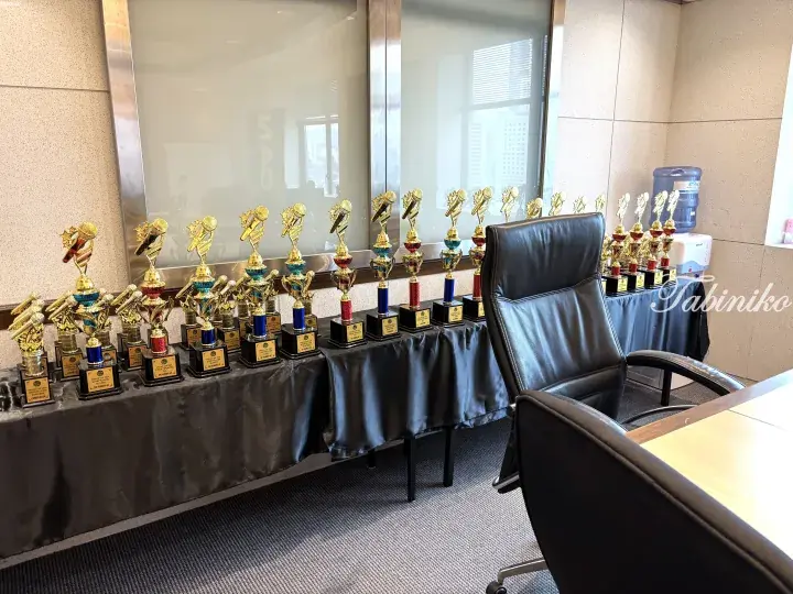 Rows of golden microphone trophies displayed on a black cloth in a modern office with a city view.