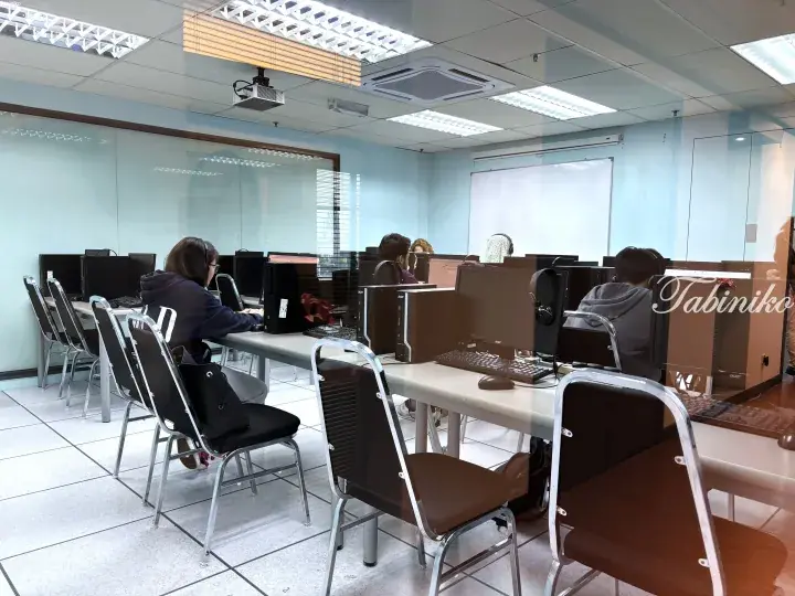 Students using desktop computers in a modern computer lab with glass walls and whiteboards.