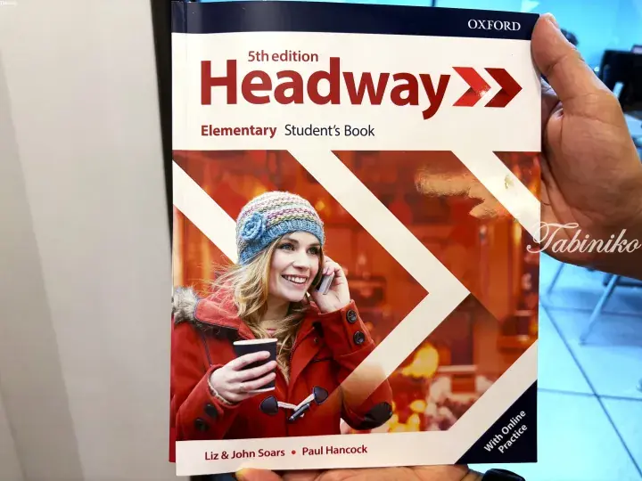 A person holding the Oxford Headway Elementary Student’s Book 5th edition textbook cover.