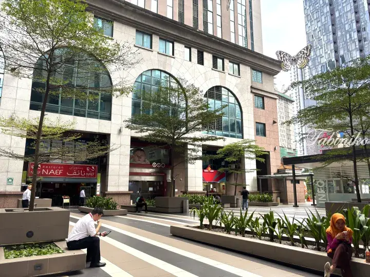 Outdoor plaza with people relaxing near a building featuring arched windows and a large butterfly sculpture.