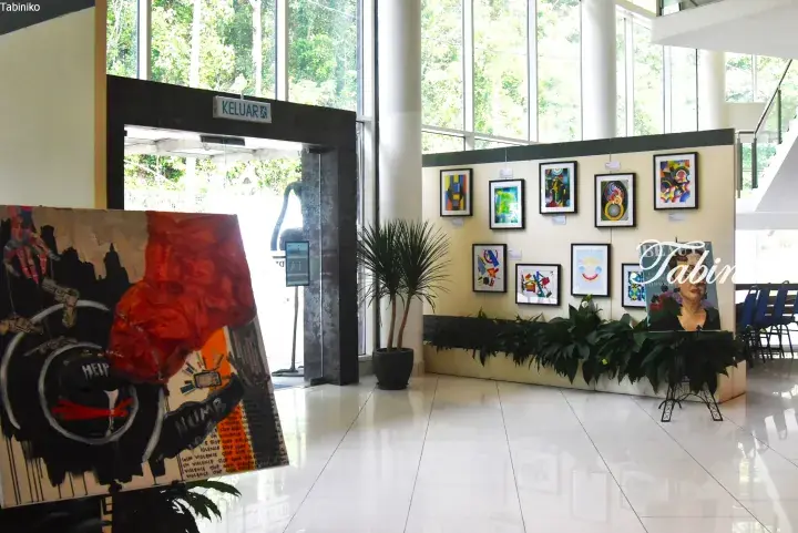 Art exhibition in a bright lobby featuring colorful abstract paintings and a mixed-media piece with gun violence awareness themes.