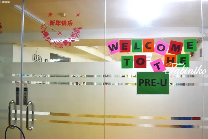 Glass door entrance to Pre-U Centre with colorful welcome sign and Chinese New Year decorations.
