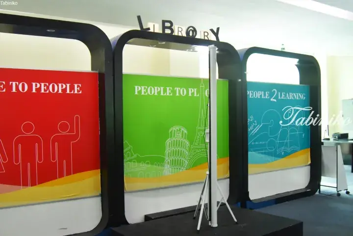 Colorful library display panels with slogans like People 2 Learning and world landmarks, featuring a tripod stand.