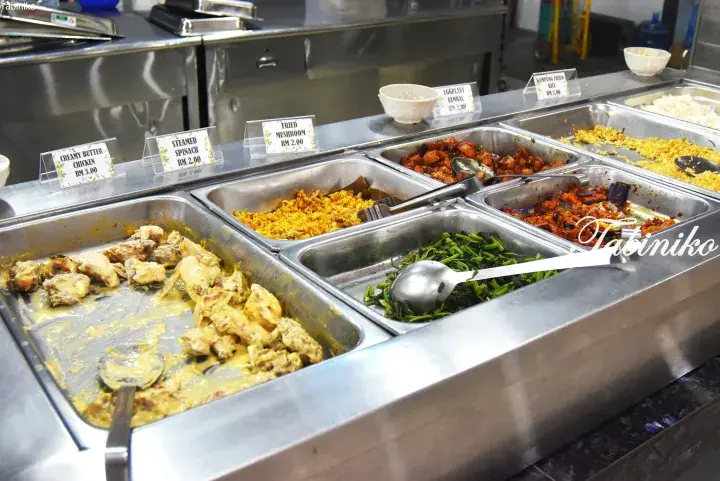Buffet trays of Malaysian dishes like creamy butter chicken, steamed spinach, and fried mushroom with price labels.