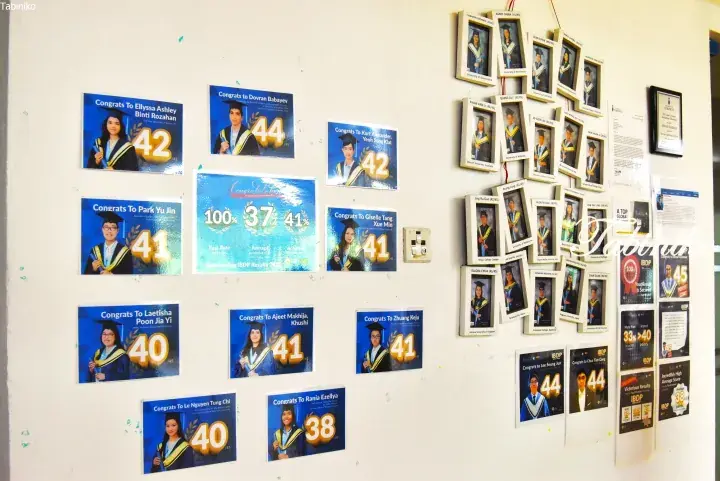 Wall displaying IBDP student achievements with high scores and university acceptance photos at a Malaysian school.