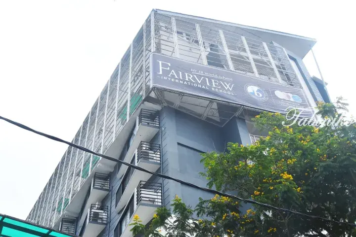 Fairview International School building facade with IB World School banner and yellow flowering trees.