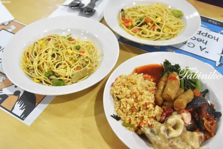 Two plates of vegetable spaghetti and a plate of Nasi Goreng with spring rolls and sambal on a wooden table.