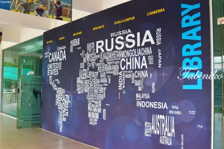 A large blue wall mural displaying a world map made of country names, with ‘LIBRARY’ written vertically in bright blue.
