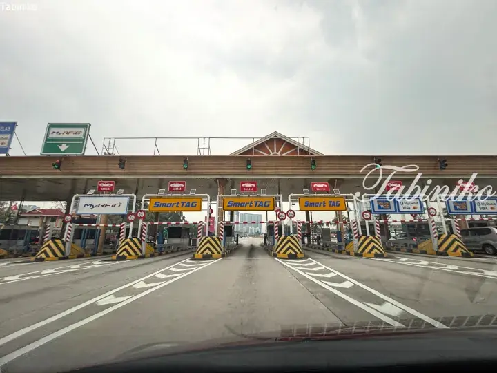 View of a Malaysian highway toll plaza with SmartTAG and MyRFID lanes under an overcast sky.