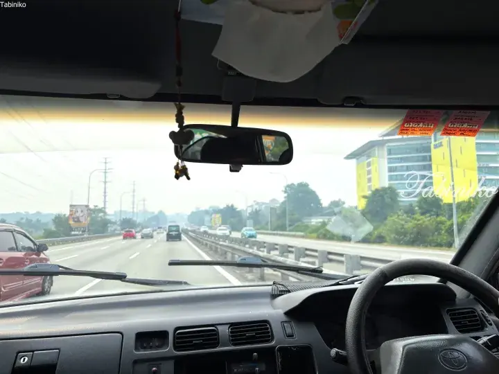 View from inside a Toyota van driving on a highway in Malaysia, showing dashboard, steering wheel, and traffic ahead.