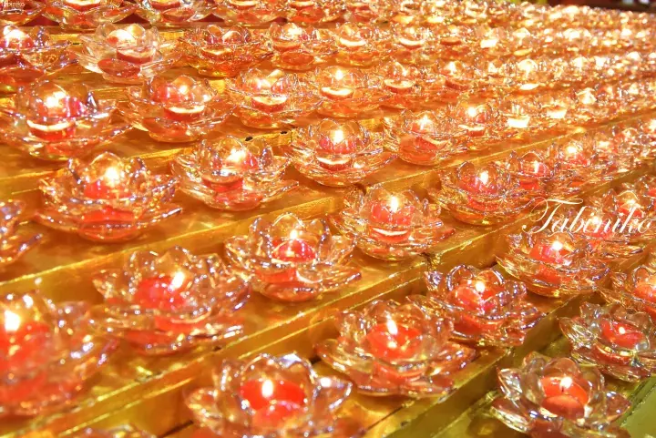 Rows of glowing lotus-shaped oil lamps on a golden shelf, creating a warm spiritual ambiance.