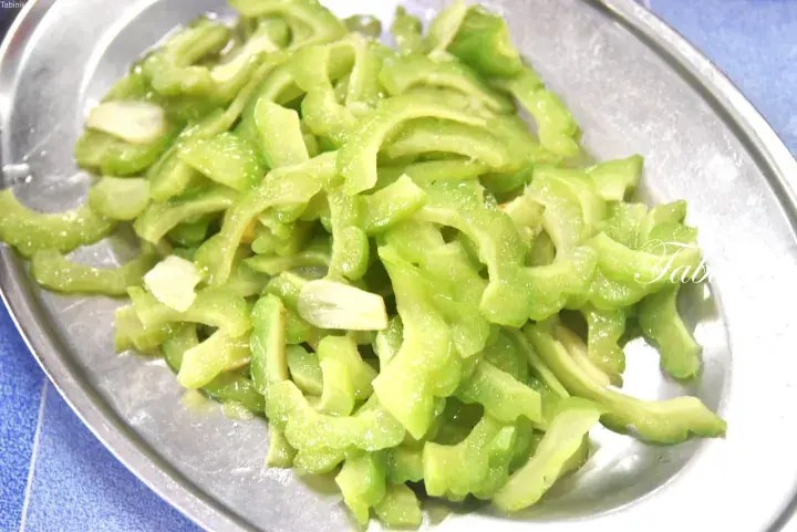 Sliced bitter melon stir-fried with garlic served on a metal plate, a common Malaysian dish.