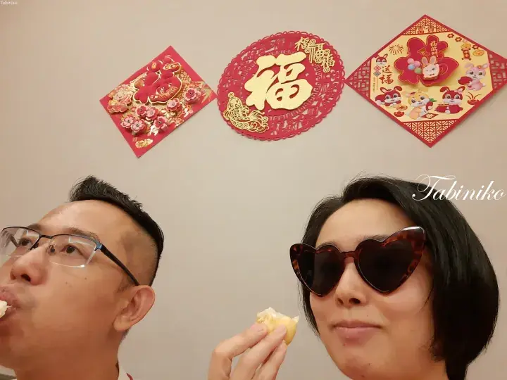 Couple enjoying food with festive Chinese New Year decorations including Fu characters and rabbit motifs on the wall behind them.