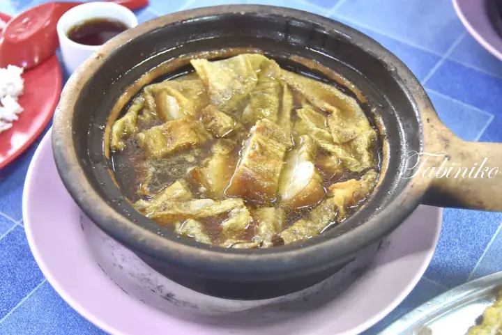 Claypot dish with braised pork and tofu skin in savory broth, served on a blue tiled table.