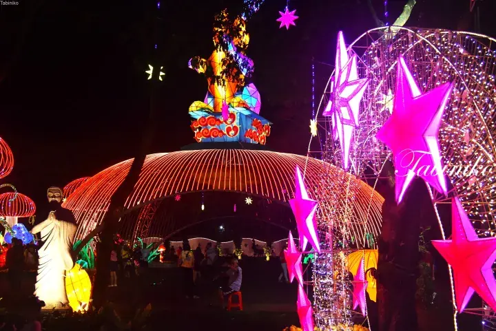 Vibrant night festival scene featuring large illuminated star lanterns and a colorful Buddha statue display.