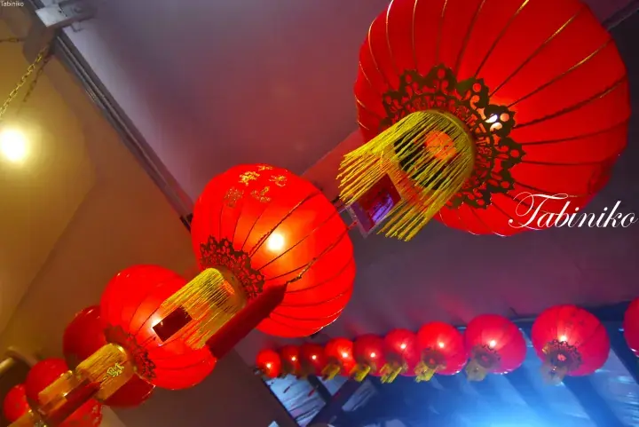 Traditional red lanterns with golden tassels hanging from a ceiling, creating a festive atmosphere.