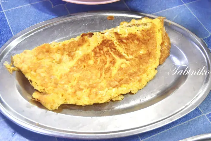 Golden omelette served on a metal plate at a traditional Malaysian restaurant.