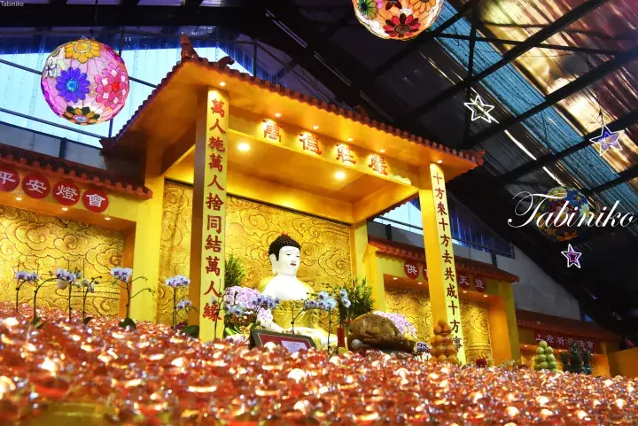 Golden Buddha statue at a Malaysian temple altar surrounded by thousands of glowing oil lamps and colorful lanterns.