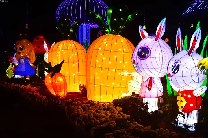 Giant illuminated lanterns of Alice in Wonderland characters and oversized carrots at a night festival in Malaysia.