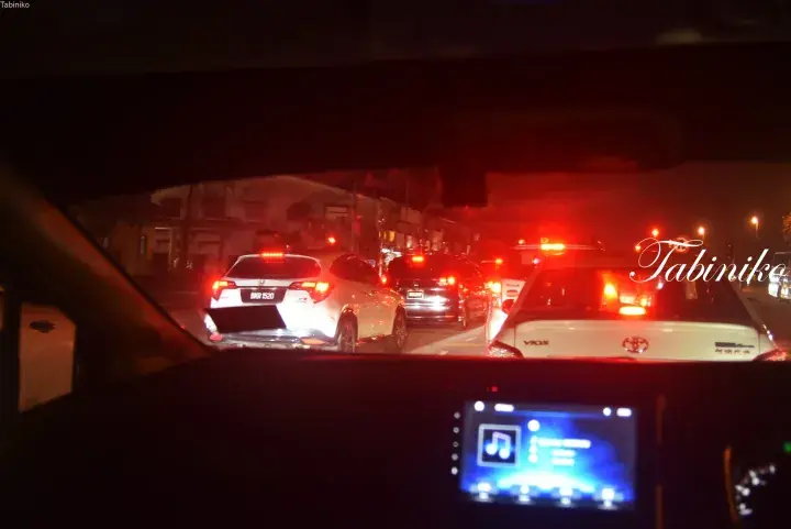 Nighttime traffic jam on a Malaysian road viewed from inside a car, showing brake lights and dashboard screen.