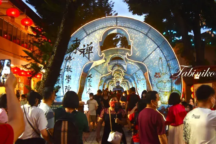 Crowd walking through a glowing Buddha-shaped tunnel at a night festival in Malaysia.