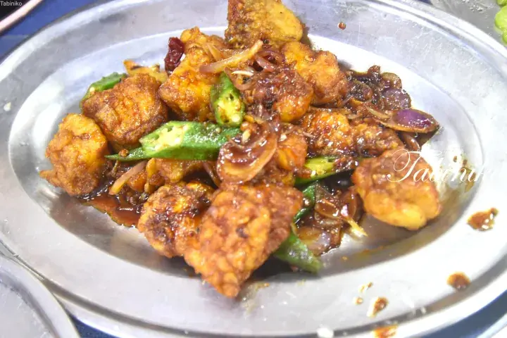 Fried tofu with okra and onions in a savory sauce served on a metal plate.